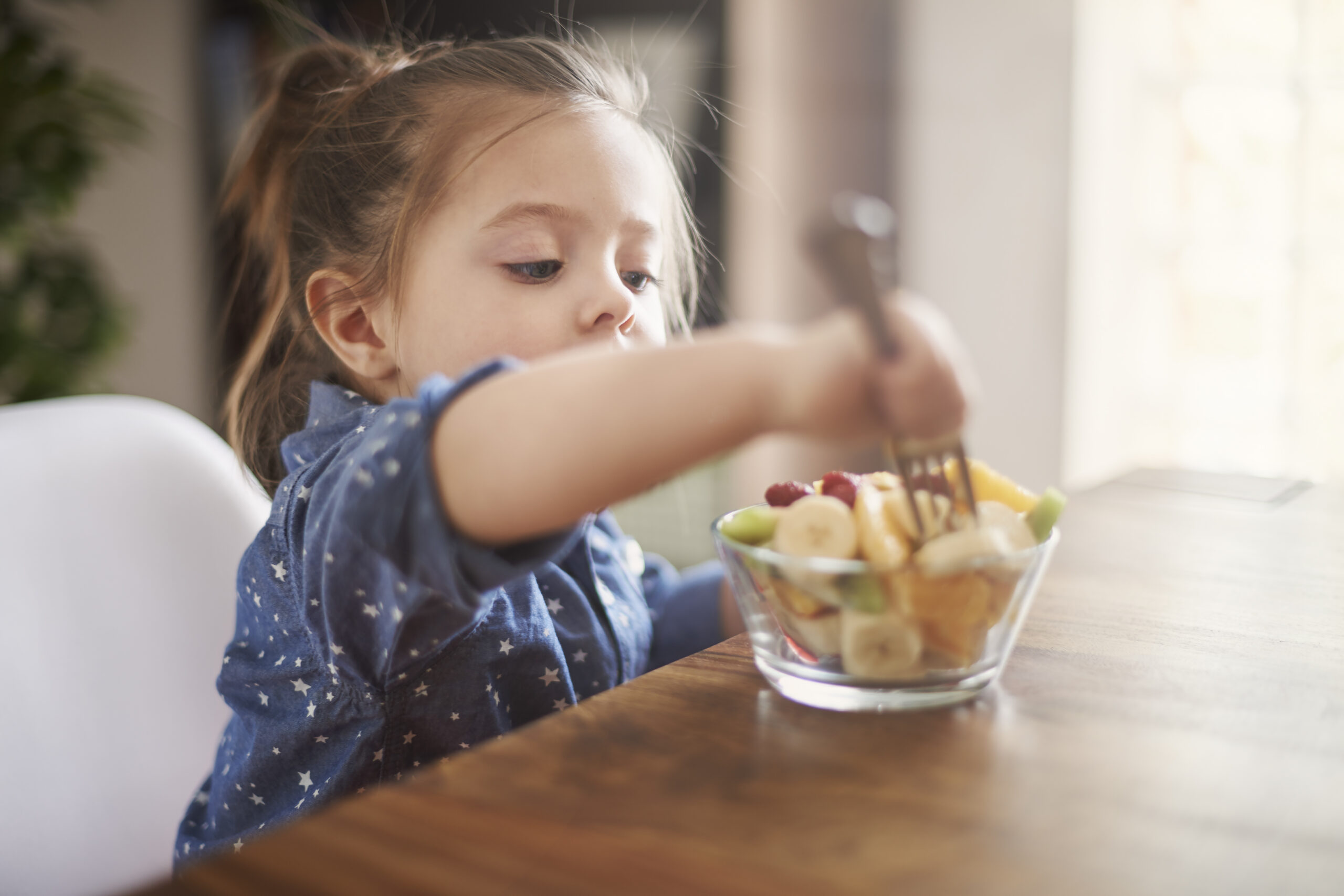Niña pequeña comiendo fruta en un cuenco con un tenedor