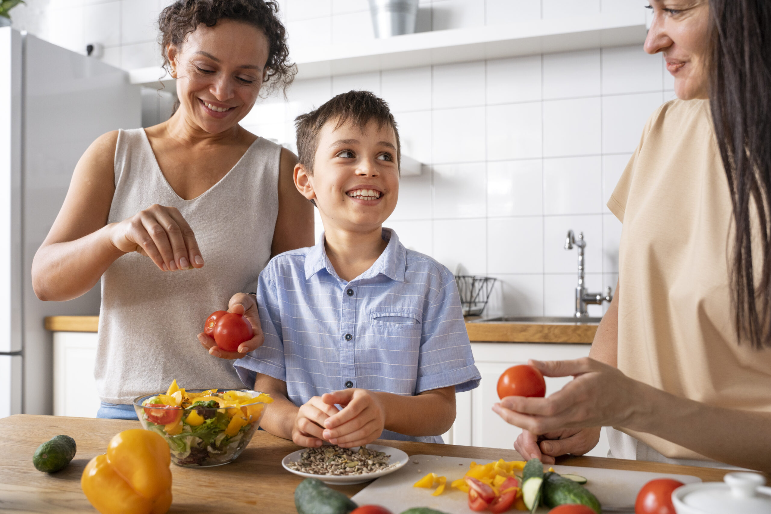 Una pareja de mujeres junto a un niño en la cocina acompañados de frutas y verduras